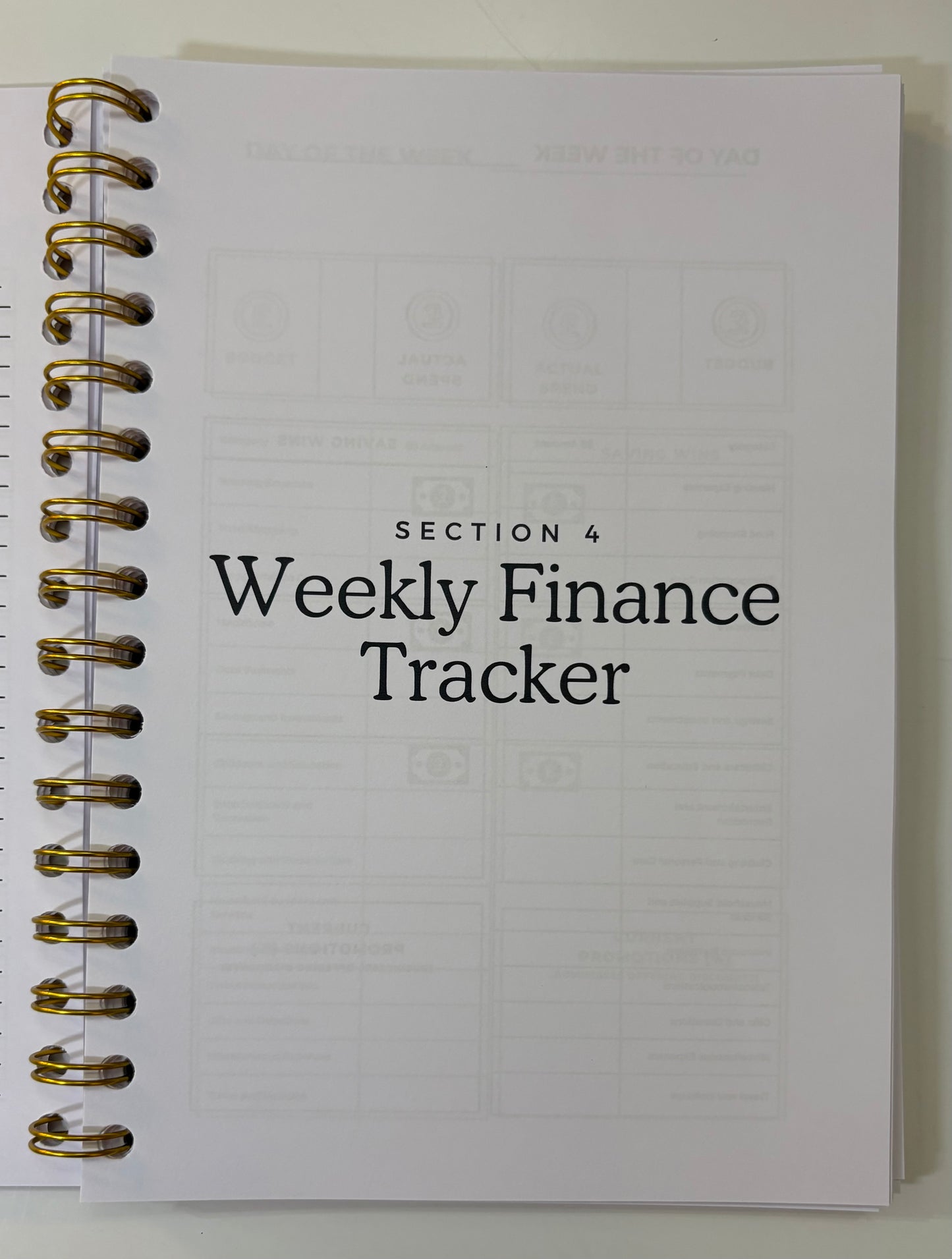 Weekly finance tracker notebook with gold spiral binding on a white background