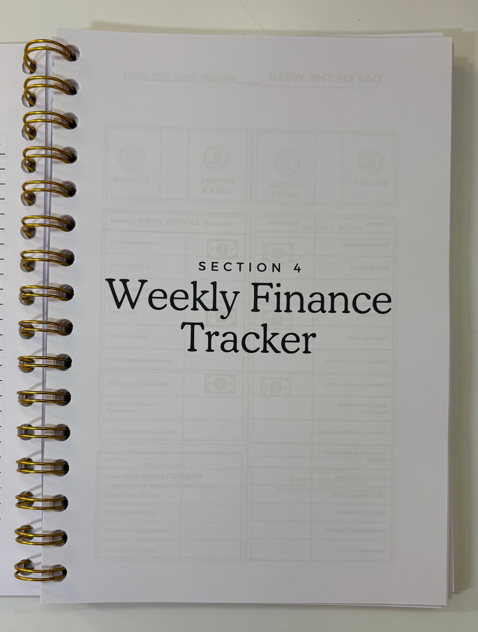 Weekly finance tracker notebook with gold spiral binding on a white background